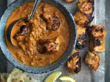 Un plat de poulet tikka savoureux, avec des morceaux de poulet grillés dans une sauce crémeuse et des accompagnements comme du pain naan et des quartiers de citron.
