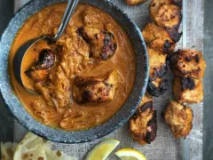 Un plat de poulet tikka savoureux, avec des morceaux de poulet grillés dans une sauce crémeuse et des accompagnements comme du pain naan et des quartiers de citron.