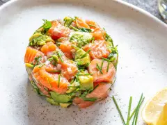 Un délicieux tartare saumon avocat, frais et coloré, garni de ciboulette et servi avec un quartier de citron.