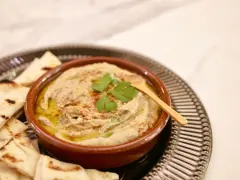 Un bol de baba ganoush crémeux, garni de persil frais et d'un filet d'huile d'olive, servi avec des pains pita grillés.