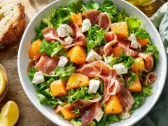 Salade melon feta avec prosciutto, roquette et laitue. Des morceaux de melon juteux, de la feta crémeuse et des tranches de prosciutto se mêlent à des feuilles vertes fraîches.