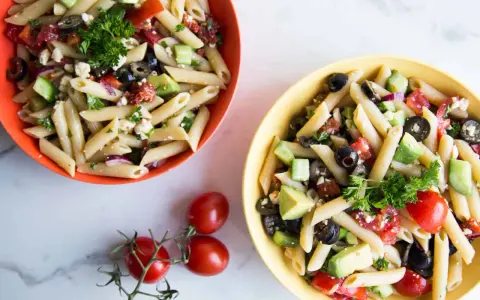 Deux bols de salade de pâtes méditerranéenne colorée, garnie de feta, olives, tomates et avocat.