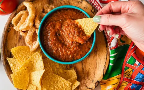Une main trempe une chips dans une sauce salsa maison. Parfait pour une sauce salsa recette rapide et savoureuse.