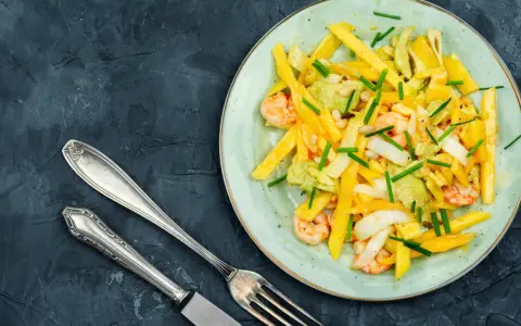 Salade colorée avec des crevettes, de l'avocat et des bâtonnets de mangue, garnie de ciboule. Un délice frais et fruité.