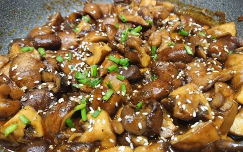 Champignons caramélisés chinois, brillants et appétissants, saupoudrés de graines de sésame et de ciboule fraîche.