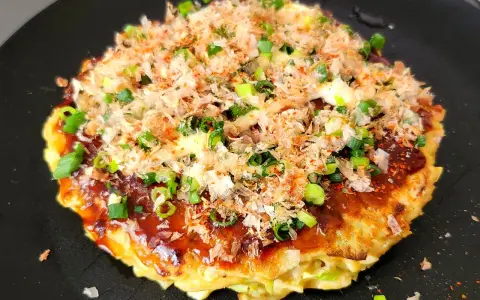 Un délicieux okonomiyaki, un plat emblématique du repas japonais maison, garni d'oignons verts et de flocons de bonite.
