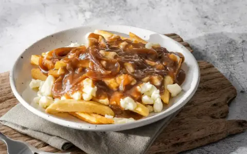 Une assiette de poutine fumante, parfaite pour une recette poutine maison facile. Des frites croustillantes, du fromage en grains et une sauce brune onctueuse.