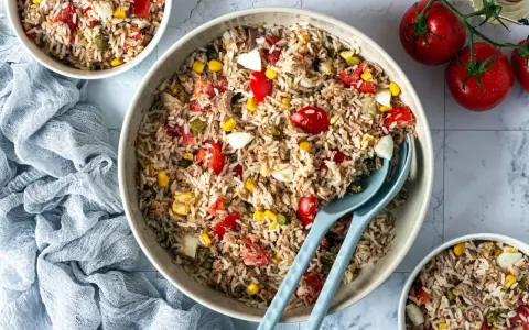 Un grand bol de salade de riz thon, garnie de tomates, maïs et œufs durs. Parfait pour un repas frais et léger.
