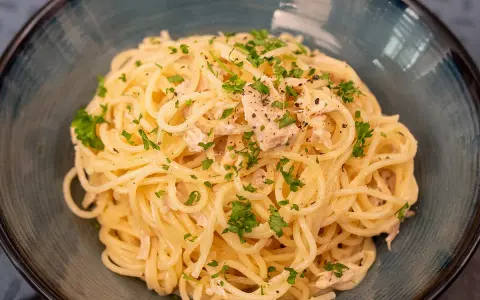 Un plat de pâtes au thon, garni de persil frais et de poivre noir, servi dans un bol bleu.