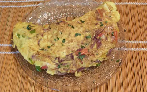 Une savoureuse omelette mexicaine garnie d'oignons rouges, de poivrons et d'herbes fraîches, servie sur une assiette en verre.