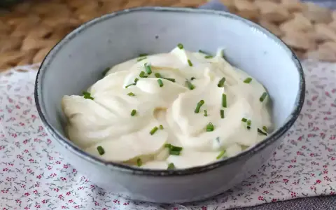 Mayonnaise sans huile crémeuse, garnie de ciboulette fraîche, dans un bol en céramique. Parfait pour un repas léger.
