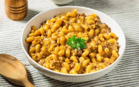 Un bol de macaroni au fromage crémeux avec du bœuf haché, garni de persil. Un plat parfait pour un dîner rapide et facile.