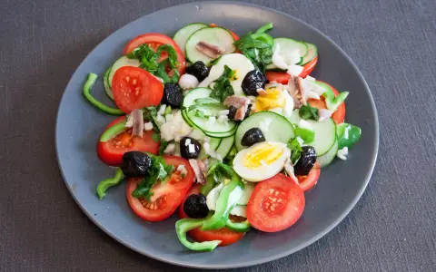Salade niçoise colorée avec tomates, concombres, œufs, olives noires et anchois.