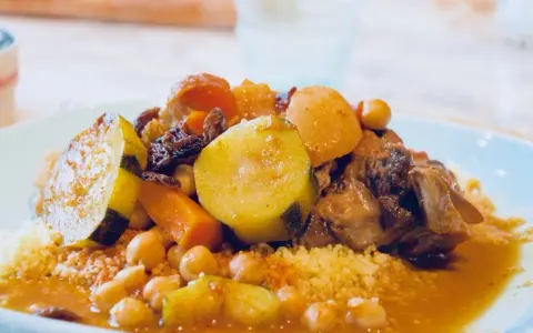 Un plat généreux de couscous algérien avec légumes, pois chiches, raisins secs et viande mijotée dans une sauce savoureuse.