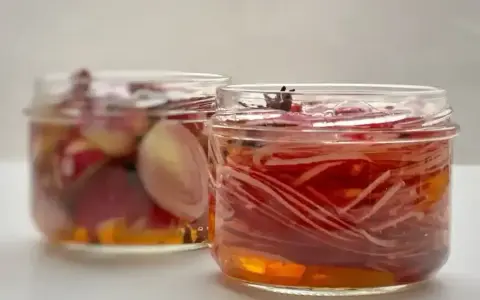 Deux bocaux de pickles d'oignon rouge, l'un avec des oignons entiers, l'autre avec des lamelles fines, baignant dans une marinade ambrée.