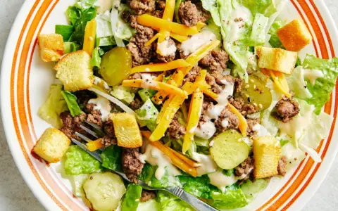 Salade Big Mac avec laitue, bœuf haché, fromage râpé, croûtons et cornichons, arrosée d'une sauce crémeuse.