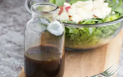 Bouteille de sauce salade facile, prête à être versée sur une salade fraîche et croquante dans un bol en verre.