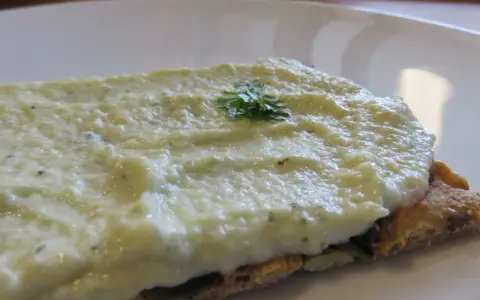 Houmous de courgette crémeux sur une tranche de pain complet, garni d'une touche de persil frais.
