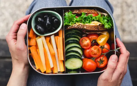 Un bento sain avec sandwich, bâtonnets de carottes et céleri, tomates cerises, concombres et olives noires.