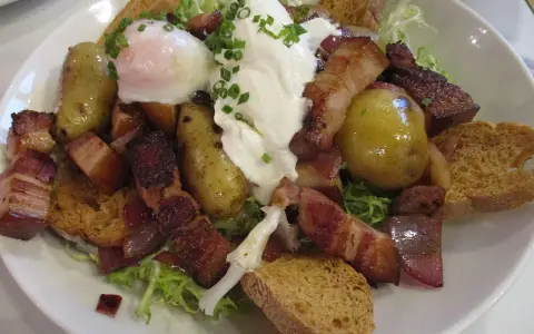 Une généreuse salade vosgienne avec des pommes de terre, lardons, œuf poché et croûtons sur un lit de verdure.