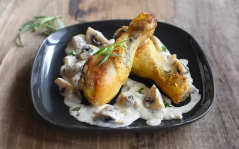 Deux pilons de poulet dorés baignent dans une sauce crémeuse aux champignons, garnie d'herbes fraîches. Un délice de poulet à la crème.