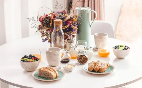 Un délicieux déjeuner vegan avec fruits frais, pain artisanal, granola et jus d'orange, présenté sur une table blanche.