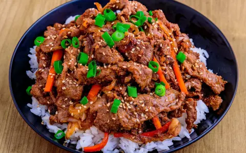 Un bol de riz blanc garni de boeuf bulgogi mariné, de julienne de carottes et d'oignons verts ciselés, parsemé de graines de sésame.