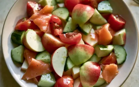 Salade fraîche et colorée : morceaux de concombre, tomates cerises, pommes rouges et saumon fumé, le tout servi dans un bol.