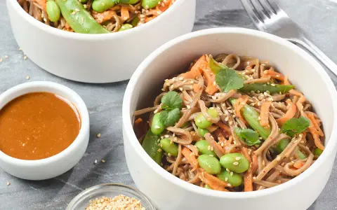Pâtes soba aux edamames, carottes râpées et coriandre, servies avec une sauce crémeuse. Un délice sain et coloré.