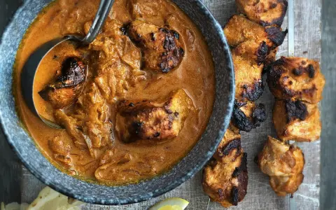Un plat de poulet tikka savoureux, avec des morceaux de poulet grillés dans une sauce crémeuse et des accompagnements comme du pain naan et des quartiers de citron.