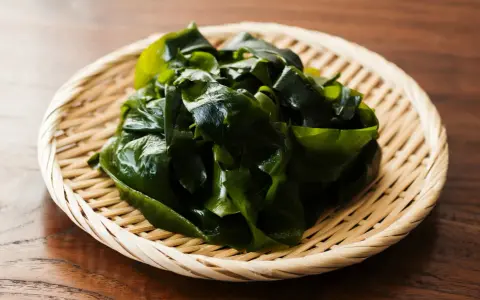 Un tas d'algue japonaise verte et brillante repose dans un panier en osier sur une table en bois.