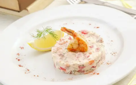 Délicieux tartare de crevette thaï, garni d'une crevette grillée et d'une tranche de citron, sur une assiette blanche.