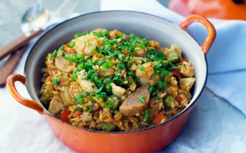 Un plat de jambalaya coloré, garni de crevettes, poulet, saucisse et oignons verts. Une recette savoureuse à découvrir.