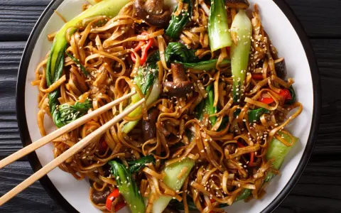 Un plat de chow mein appétissant avec des nouilles, des légumes verts croquants, des champignons et des poivrons rouges, saupoudré de graines de sésame.