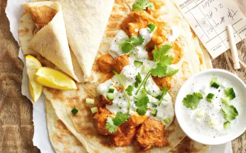 Un plat de butter chicken crémeux servi sur du pain naan avec du raïta et des quartiers de citron.