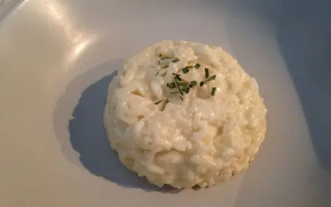 Un crémeux risotto coco, parsemé de ciboulette fraîche, repose sur une assiette claire.
