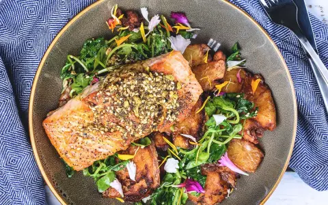 Un filet de saumon croustillant, garni de graines, servi avec des pommes de terre rôties et une salade verte. Un accompagnement poisson savoureux et coloré.