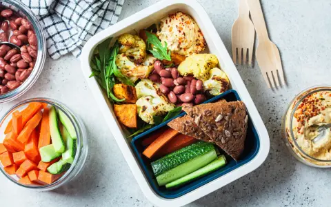 Un repas tiré du sac sain et coloré : houmous, légumes rôtis, haricots rouges, pain complet et crudités. Parfait pour un déjeuner sur le pouce.