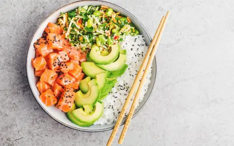 Un délicieux poke bowl santé avec saumon cru, avocat, riz blanc et légumes croquants, prêt à être dégusté avec des baguettes.