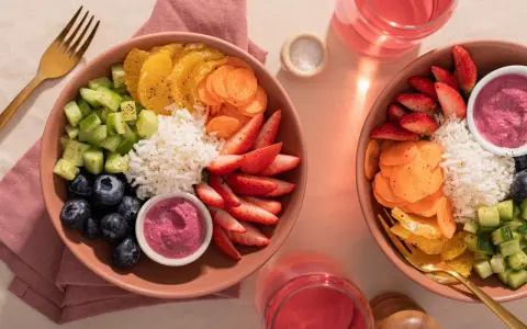 Deux bols colorés remplis de riz, fraises, myrtilles, concombre, carottes et oranges. Une belle idée poke bowl pour un repas frais et sain.