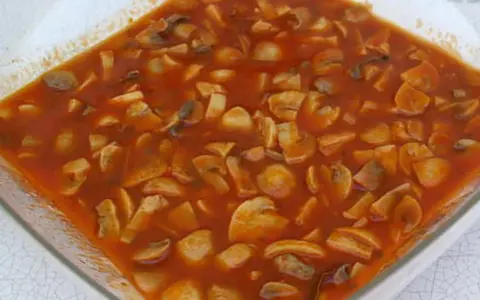 Champignons à la grecque, une préparation savoureuse de champignons coupés en morceaux, mijotant dans une sauce tomate riche et parfumée.