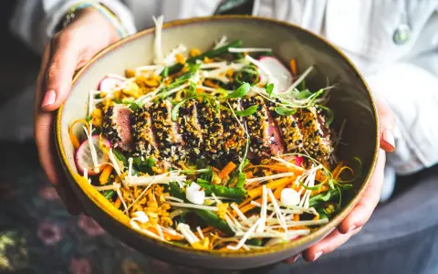 Un délicieux tataki de thon, enrobé de sésame, servi avec un accompagnement coloré de légumes croquants et de pousses fraîches.