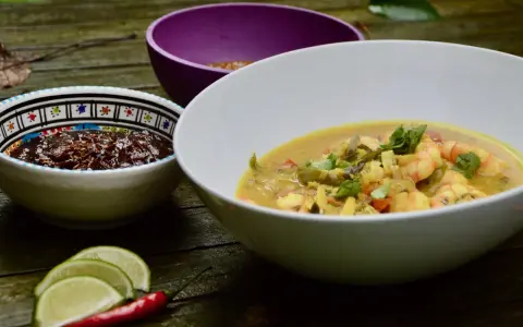 Un plat de crevette curry coco crémeux, garni de coriandre fraîche, servi avec des quartiers de citron vert et un piment rouge.