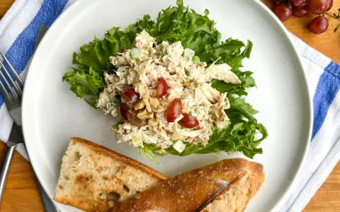 Salade de poulet froid mayonnaise sur laitue, avec des raisins et des noix, servie avec du pain croustillant.