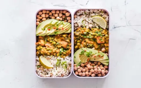 Deux lunch box remplies d'une idée lunch box école saine : curry de légumes, riz, pois chiches et avocat.