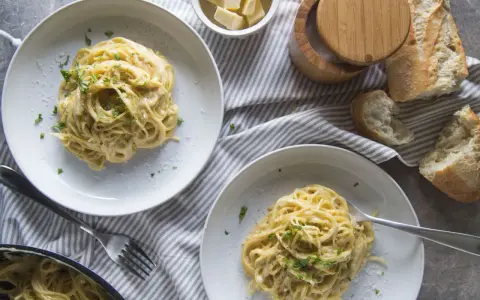Deux assiettes de pâtes crémeuses à l'ail, garnies de persil frais. Un pain croustillant et du fromage râpé complètent cette recette de pâtes à l'ail et crème.