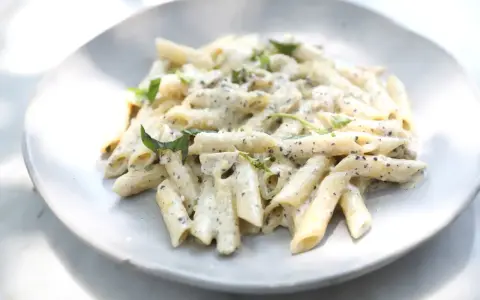 Pâtes penne nappées d'une sauce crémeuse à l'ail, parsemées de fines herbes fraîches, servies sur une assiette blanche.