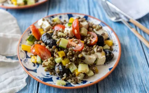 Salade de lentilles colorée avec tomates, concombre, poivrons, olives noires et feta. Un plat frais et savoureux.