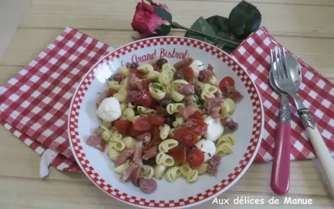 Une savoureuse salade italienne de pâtes avec tomates cerises, mozzarella, olives et jambon cru, garnie de ciboulette.