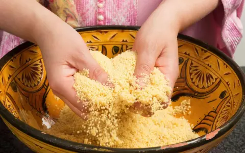 Mains travaillant du couscous marocain dans un plat traditionnel décoré.
